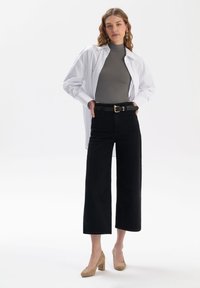 Biała koszula z długim rękawem na szarym dopasowanym topie, połączona z czarnymi szerokimi spodniami o wysokim stanie i beżowymi butami na słupku.