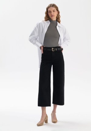 Biała koszula z długim rękawem na szarym dopasowanym topie, połączona z czarnymi szerokimi spodniami o wysokim stanie i beżowymi butami na słupku.