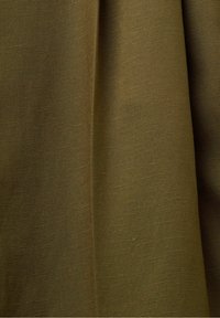 Gros plan sur un tissu vert olive avec une couture verticale et une texture fine visible, montrant un drapé souple et des ombres subtiles.