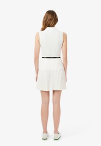 Witte geplooide jurk met een mouwloos ontwerp en een zwarte leren riem met merklogo. De stof lijkt glad met een lichte, vloeiende textuur.