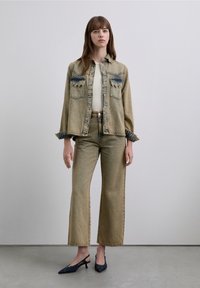 Jachetă din denim cu accente albastre, asortată cu pantaloni largi din denim. Culoare bej, croială lejeră și detalii contrastante de cusătură.