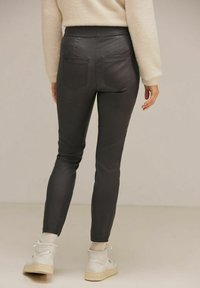 Grå slim-fit byxor med en slät textur, med bakfickor och hög midja, i kombination med vita högstegade sneakers.