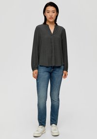 Haut à manches longues noir à motifs avec un col en V, accompagné d'un jean bleu et de baskets blanches, créant une tenue décontractée.