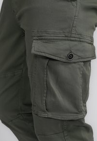 Olijfgroene cargobroeken van stof hebben een zijzak met een klep en knoopsluiting, een soepele textuur en versterkte stikseldetails.