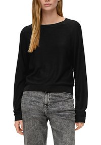 Schwarzer, langärmeliger Pullover mit weitem Ausschnitt und gerippten Bündchen, kombiniert mit hellgrauen Jeans. Der Pullover hat eine lockere Passform und eine glatte Textur.
