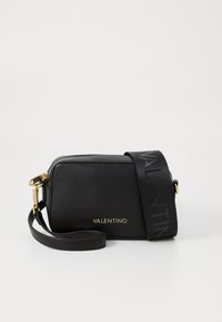 Sac en cuir noir à bandoulière avec un logo doré, fermeture éclair et une bandoulière noire ornée d'un motif de logo répétitif. Forme rectangulaire compacte.
