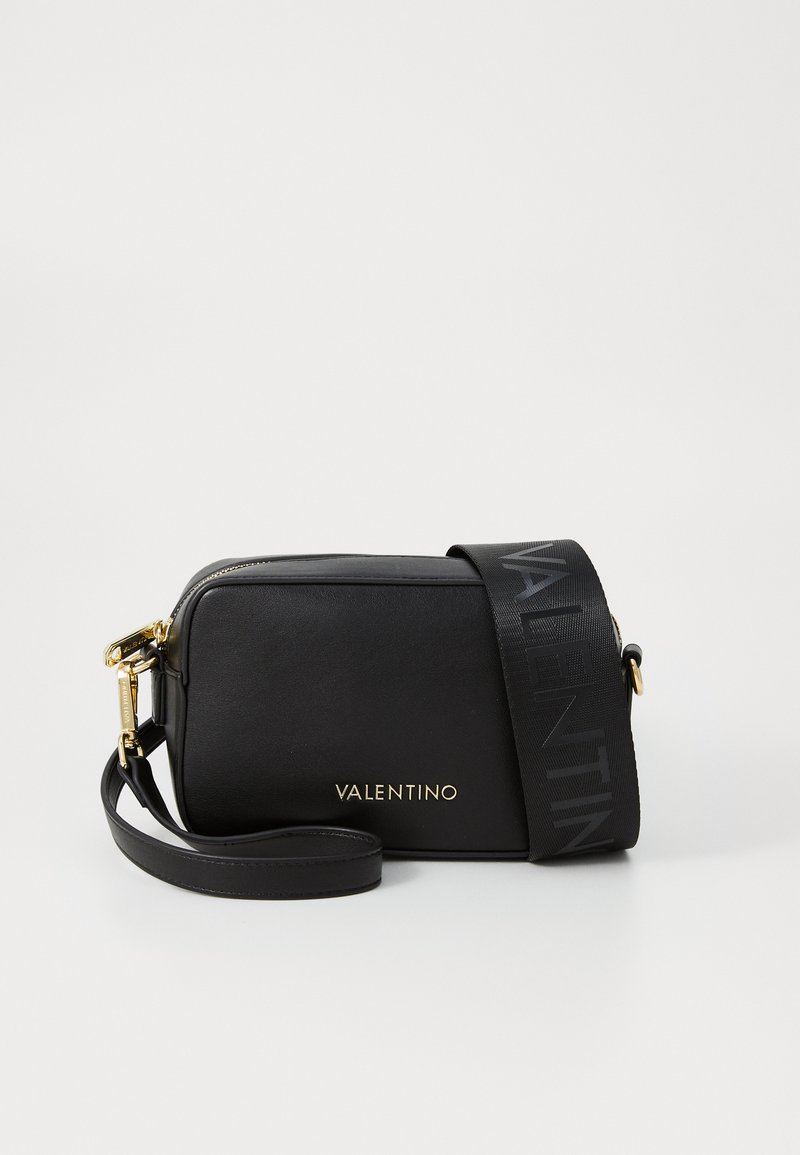 Sac en cuir noir à bandoulière avec un logo doré, fermeture éclair et une bandoulière noire ornée d'un motif de logo répétitif. Forme rectangulaire compacte.