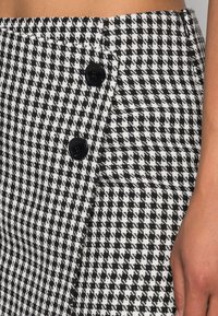 Gonna a scacchi bianco e nero con un tessuto testurizzato, bottoni laterali e una silhouette aderente con uno spacco.