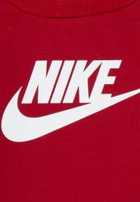 Κόκκινη βαμβακερή μπλούζα με λευκό λογότυπο Nike και γραφιστικό σχέδιο swoosh. Ομαλή υφή, στρογγυλή λαιμόκοψη, χωρίς επιπλέον σχέδια ή διακοσμητικά στοιχεία.