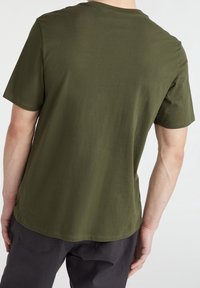 T-shirt de algodón de manga corta en verde oliva, con cuello redondo y un corte relajado, de textura suave y lisa, sin logotipos visibles.