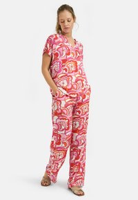 Dwuczęściowy zestaw w kwiatowy wzór w odcieniach różu i czerwieni, z krótkimi rękawami, topem w serek oraz szerokimi spodniami z kieszeniami po bokach. Gładka tekstura materiału.