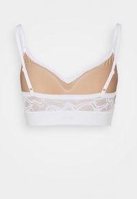 Lichte bralette met een nude binnenvoering, witte kantband met golfpatroon en verstelbare witte schouderbanden; zachte textuur.