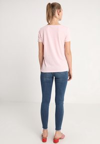 Top de manga corta de color rosa claro con un diseño sencillo, combinado con jeans de mezclilla azul oscuro. Los jeans tienen un ligero estiramiento y una textura desgastada.