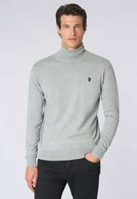 Maglione a collo alto grigio chiaro realizzato in un morbido tessuto a maglia. Presenta un design aderente, maniche lunghe e un piccolo logo ricamato sul petto.