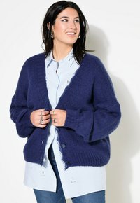 Navy gebreide cardigan met een ruime pasvorm, textuurstof en een open voorkant. Gecombineerd met een lichtblauw overhemd met knopen en denim jeans.