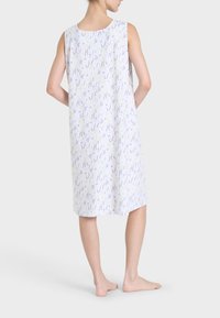 Vestaglia senza maniche realizzata in tessuto leggero con motivo floreale che presenta accenti di lavanda e giallo. Sfondo bianco, taglio fino al ginocchio.