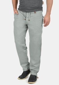 Pantalon en coton gris clair à coupe décontractée, taille à cordon, poches latérales et couture simple ; porté avec des sabots noirs.