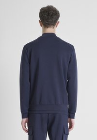 Sudadera azul marino con mangas largas, puños y dobladillo de canalé. El diseño presenta un cuello alzado y una textura suave y lisa.