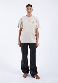 Béžové bavlněné tričko s krátkými rukávy a motivem srdce na levé straně hrudi. Párek tmavě šedých rozšířených džínů s volnějším střihem.