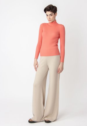 Rullekrave sweater i koralfarvet ribstrik, parret med brede beige bukser i et blødt stof, der har en afslappet silhuet.