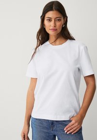 Camiseta de algodón blanca con cuello redondo y mangas cortas, con un corte relajado y textura suave, combinada con jeans de denim azul.
