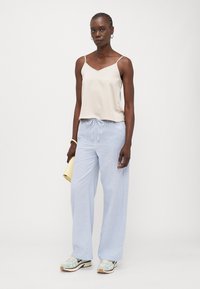 Beige satin camisole with thin straps, paired with light blue, loose-fitting pants. Accessories include a yellow clutch and multi-colored sneakers.