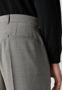 Kockované nohavice z čierno-bielej látky, s priliehavým strihom a detailom zadnej vrecka, skombinované s čiernym topom.