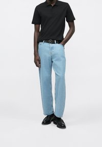 Czarna koszulka polo, jasnoniebieskie jeansy o prostych nogawkach, czarny pasek i czarne buty. Prosty design i luźny krój.