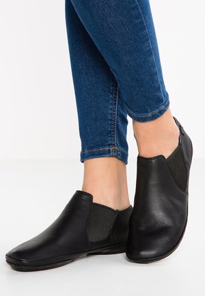 Chaussures noires à enfiler en cuir avec des panneaux élastiques sur les côtés. Bout arrondi et semelle plate, associées à un jean skinny bleu.