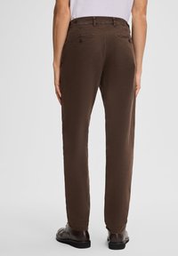 Bruine broek van lichtgewicht stof, met een rechte pasvorm. Twee achterzakken met knoopsluitingen en een gladde textuur.