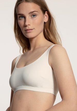 Bralette beige chiaro con scollatura a forma di U e spalline sottili. Tessuto liscio e design senza cuciture, con una morbida fascia elastica sotto.