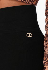 Black ribbed leggings feature a thick waistband and a gold hardware accent on the side. The texture is smooth with a slight stretch.