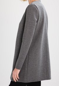 Cappotto grigio con texture, maniche lunghe, vestibilità comoda e un motivo unico. Presenta un collo tondo e un orlo dritto.