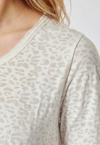 Top beige clair en tissu transparent avec un subtil motif léopard, col rond et texture douce.