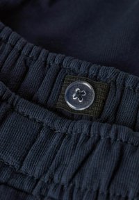 Ceinture en tissu bleu marine avec une texture plissée, dotée d'un bouton en plastique transparent et d'un band élastique noir pour un ajustement réglable.