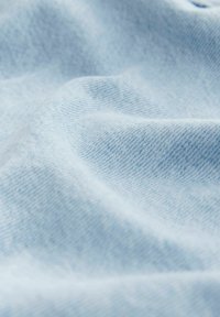 Tela de mezclilla azul claro con una textura suave, que presenta un sutil tejido diagonal y ligeras arrugas, enfatizando una apariencia casual.