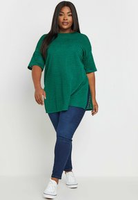 Grön texturerad topp med korta ärmar och rundad halsringning, i kombination med mörkblå smala jeans och vita sneakers.