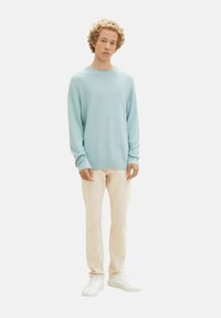 Maglione azzurro chiaro a coste con maniche lunghe, abbinato a pantaloni beige chiaro e sneakers bianche. Design semplice, texture morbida, vestibilità casual.