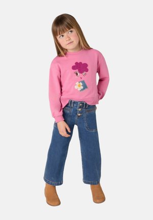 Felpa rosa con design di fiori e toppe in denim, abbinata a jeans a vita alta a zampa d'elefante e stivaletti alla caviglia marroni. Tessuto dalla superficie liscia.