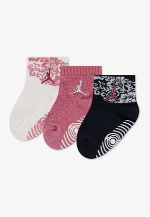 Trois chaussettes pour bébé en blanc, rose et noir, chacune avec des motifs décoratifs et un petit logo Jumpman au niveau de la cheville.