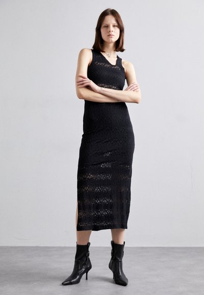 Svart blonde midi kjole med ermeløs design, med en teksturert mønster og sidelommer, kombinert med spisse svarte hæl støvler.