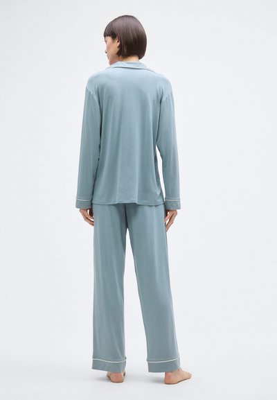 Világoskék pizsamaszett puha anyagból; hosszú ujjú, gombos felsőből és laza szabású nadrágból áll, amelyek mandzsettáin kontrasztos szegéllyel rendelkeznek.