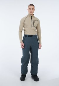 Beige fleece pullover met kwart-zip en zwarte accentstiksels, gecombineerd met donkerblauwe waterdichte broek, uitgerust met een riem en zakdetails.