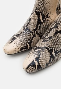 Bottes à bout pointu avec motif en peau de serpent beige et noir, montrant une surface texturée et des écailles détaillées sur fond blanc.