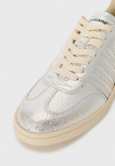 Silver sneaker with a cracked leather texture, beige laces, rubber sole, and striped design details on the sides.