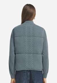 Blaues gepolstertes Sweatshirt mit hohem Kragen. Strukturierter Zopfmuster-Look verläuft vertikal über den Rücken und hat gerippte Bündchen und einen gerippten Saum.