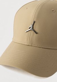 Καφέ καπέλο μπέιζμπολ με υφή, το οποίο διαθέτει μεταλλικό ασημί λογότυπο Jumpman στο μπροστινό μέρος. Διατηρεί δομημένο σχήμα και καμπυλωτό γείσο.