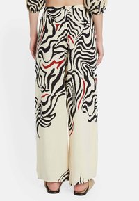 Pantalones de pierna ancha en un crema claro con un patrón en espiral en negro y rojo. Están hechos de una tela suave con una textura fluida.