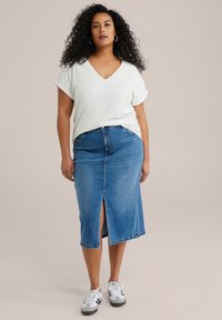 Top bianco strutturato a V abbinato a una gonna di jeans lunghezza ginocchio con spacco frontale, indossato con scarpe da ginnastica nere e bianche casual.