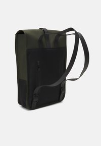 Vertikal ryggsäck i slitstarkt tyg, med en mörkgrön topp och svart frontpanel, smal form och justerbara svarta remmar.